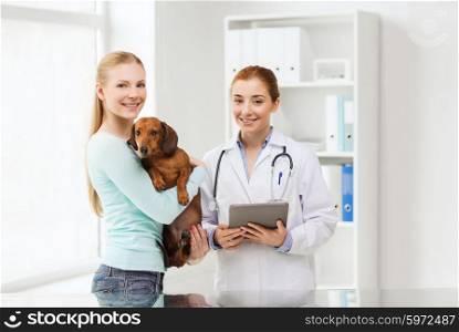 medicine, pet, health care, technology and people concept - happy woman holding dachshund dog and veterinarian doctor with tablet pc computer at vet clinic