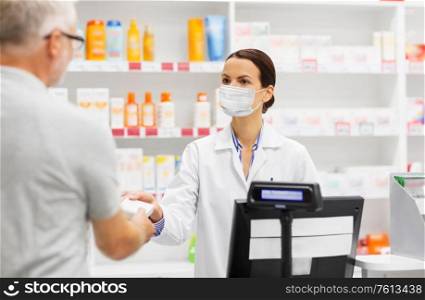 medicine, pharmaceutics and healthcare concept - apothecary wearing face protective medical mask for protection from virus disease and senior man customer buying drug at pharmacy. apothecary in mask and senior customer at pharmacy