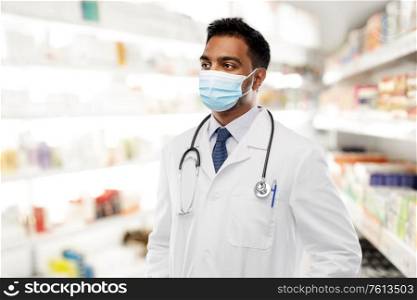 medicine, pharmaceutics and healthcare concept - indian male doctor or pharmacist with stethoscope wearing face protective medical mask for protection from virus disease over pharmacy on background. indian male doctor in medical mask at pharmacy