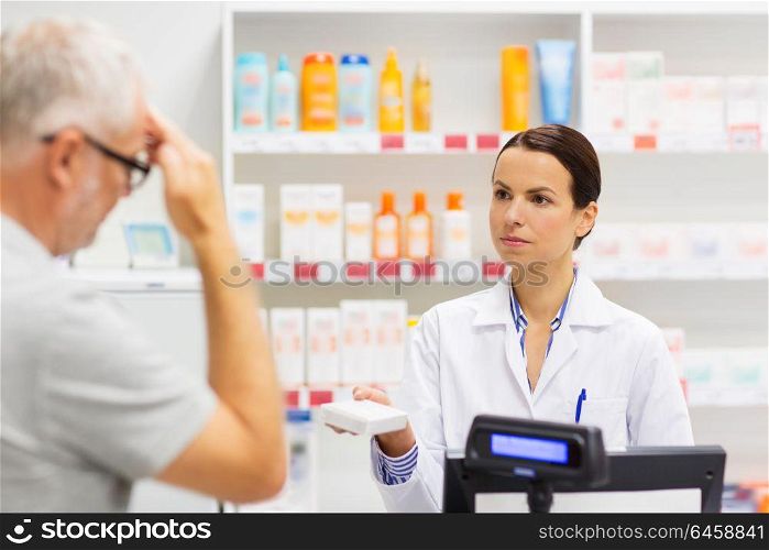 medicine, pharmaceutics, health care and people concept - apothecary giving analgetic drug to senior man customer with headache at drugstore. apothecary giving drug to senior man at pharmacy
