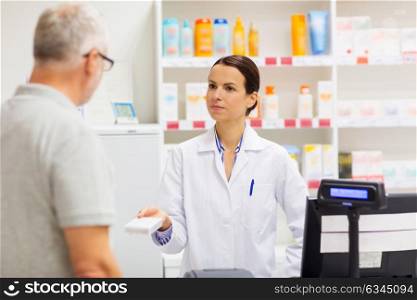 medicine, pharmaceutics, health care and people concept - apothecary giving drug to senior man customer at drugstore. apothecary showing drug to senior man at pharmacy