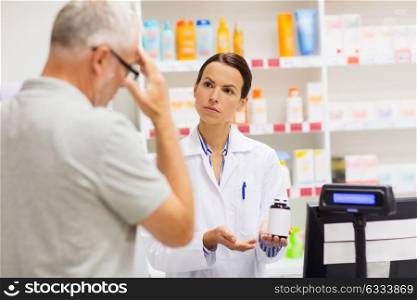 medicine, pharmaceutics, health care and people concept - apothecary showing analgetic drug to senior man customer with headache at drugstore. apothecary showing drug to senior man at pharmacy