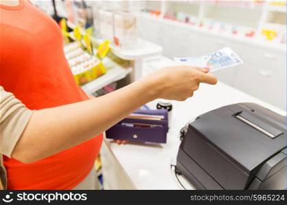 medicine, pharmaceutics, health care and people concept - close up of pregnant woman giving money and buying medication at cash register in drugstore