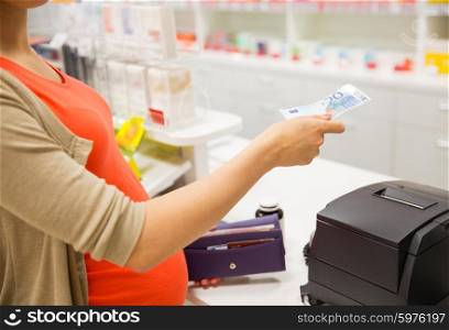 medicine, pharmaceutics, health care and people concept - close up of pregnant woman giving money and buying medication at cash register in drugstore