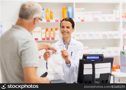 medicine, pharmaceutics, health care and people concept - female apothecary giving senior male customer his purchase in bag at drugstore. apothecary selling drug to senior man at pharmacy