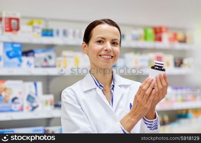 medicine, pharmaceutics, health care and people concept - happy female pharmacist with drug jar at pharmacy