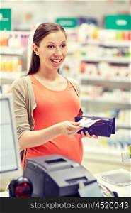 medicine, pharmaceutics, health care and people concept - happy pregnant woman with wallet in at cash register drugstore