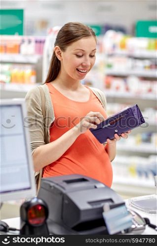 medicine, pharmaceutics, health care and people concept - happy pregnant woman with wallet in at cashbox drugstore