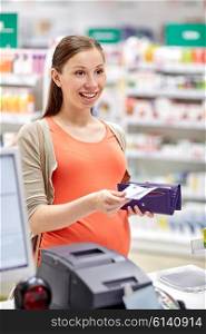 medicine, pharmaceutics, health care and people concept - happy pregnant woman with wallet in at cash register drugstore