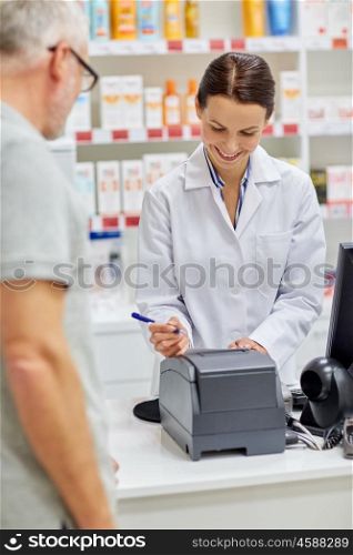 medicine, pharmaceutics, health care and people concept - smiling pharmacist writing check and senior man at drugstore cash register