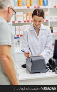 medicine, pharmaceutics, health care and people concept - smiling pharmacist writing check and senior man at drugstore cash register