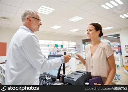 medicine, pharmaceutics, health care and people concept - smiling woman with wallet giving money to senior man pharmacist at drugstore cash register