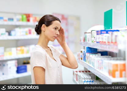 medicine, pharmaceutics, healthcare and people concept - female customer having headache choosing drugs at pharmacy. customer with headache choosing drugs at pharmacy