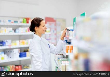 medicine, pharmaceutics, healthcare and people concept - happy female apothecary taking drug from shelf at pharmacy. happy female apothecary with drug at pharmacy. happy female apothecary with drug at pharmacy