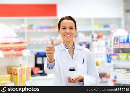 medicine, pharmaceutics, healthcare and people concept - happy female apothecary with drug showing thumbs up at pharmacy. apothecary with drug showing thumbs up at pharmacy
