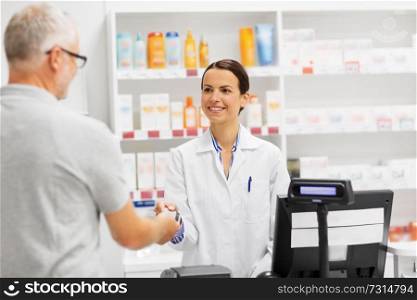 medicine, pharmaceutics, healthcare and people concept - happy smiling female apothecary taking senior customer credit card at pharmacy cash register. apothecary taking customer credit card at pharmacy
