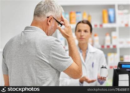 medicine, pharmaceutics, healthcare and people concept - pharmacist showing drug to senior man customer at drugstore. pharmacist and old man with medicine at pharmacy