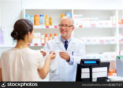 medicine, pharmaceutics, healthcare and people concept - senior apothecary with drug and female customer at pharmacy. apothecary with cure and customer at pharmacy