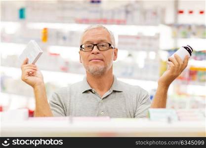 medicine, pharmaceutics, healthcare and people concept - senior male customer choosing between drugs at pharmacy. senior male customer choosing drugs at pharmacy