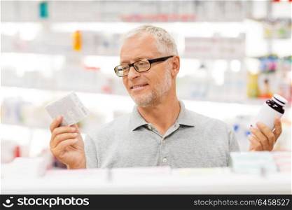 medicine, pharmaceutics, healthcare and people concept - senior male customer choosing between drugs at pharmacy. senior male customer choosing drugs at pharmacy