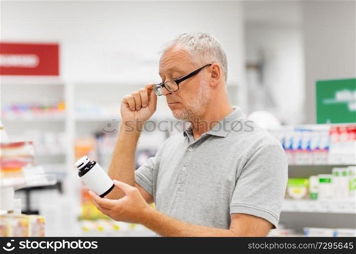 medicine, pharmaceutics, healthcare and people concept - senior male customer reading label on jar of drug at pharmacy. senior male customer with drug at pharmacy