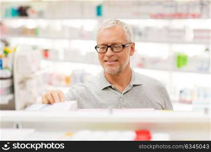 medicine, pharmaceutics, healthcare and people concept - senior male customer with drug at pharmacy. senior male customer with drug at pharmacy