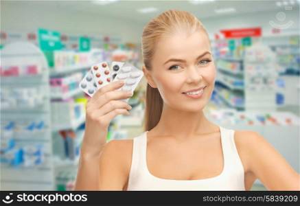 medicine, pharmacy, people, health care and pharmacology concept - happy young woman with variety of pills over drugstore background