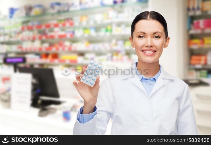 medicine, pharmacy, people, health care and pharmacology concept - happy young woman pharmacist with pills over drugstore background