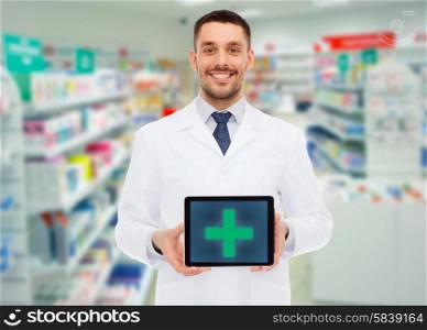 medicine, pharmacy, people, health care and pharmacology concept - smiling male doctor showing tablet pc computer with cross symbol on screen over drugstore background