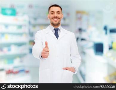 medicine, pharmacy, people, health care and pharmacology concept - smiling male pharmacist in white coat showing thumbs up over drugstore background