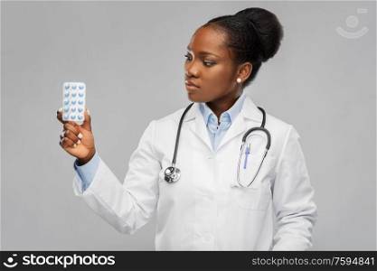 medicine, profession and healthcare concept - african american female doctor or in white coat with pills and stethoscope over background. african american female doctor with medicine pills