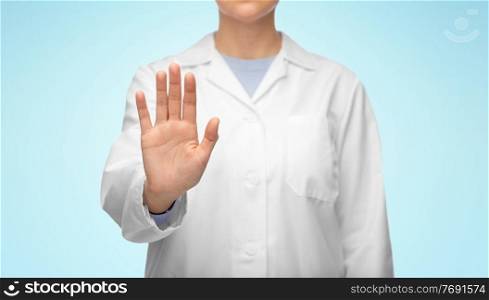 medicine, profession and healthcare concept - close up of female doctor in white coat showing stop gesture over blue background. female doctor in white coat showing stop gesture
