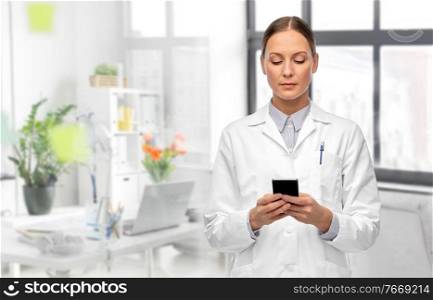 medicine, profession and healthcare concept - female doctor with stethoscope using smartphone over medical office at hospital on background. female doctor with smartphone at hospital