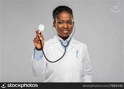 medicine, profession and healthcare concept - happy smiling african american female doctor in white coat with stethoscope over background. african american female doctor with stethoscope