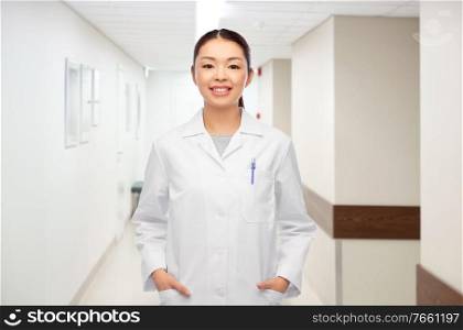 medicine, profession and healthcare concept - happy smiling asian female doctor in white coat over hospital background. happy smiling asian female doctor at hospital