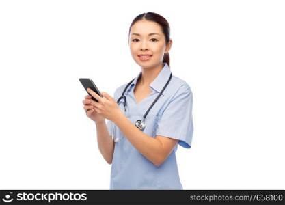medicine, profession and healthcare concept - happy smiling asian female doctor or nurse in blue uniform with stethoscope using smartphone over white background. happy asian female doctor or nurse with smartphone
