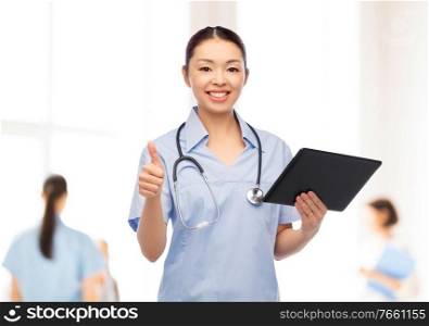 medicine, profession and healthcare concept - happy smiling asian female doctor or nurse with tablet pc computer and stethoscope showing thumbs up over hospital background. nurse with tablet pc shows thumbs up at hospital
