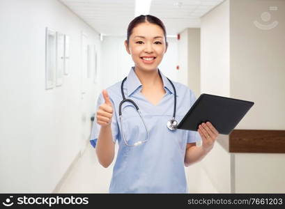 medicine, profession and healthcare concept - happy smiling asian female doctor or nurse with tablet pc computer and stethoscope showing thumbs up over hospital background. nurse with tablet pc shows thumbs up at hospital