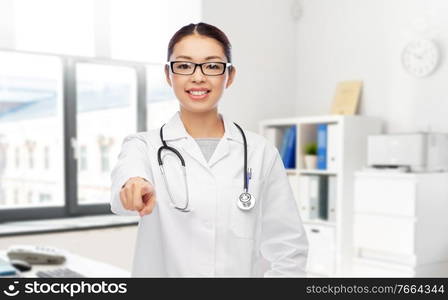 medicine, profession and healthcare concept - happy smiling asian female doctor or nurse with stethoscope pointing to camera over hospital background. asian female doctor pointing to you at hospital