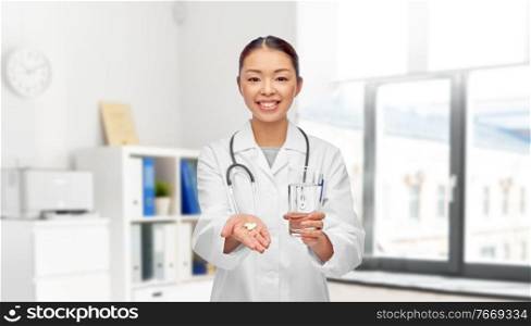 medicine, profession and healthcare concept - happy smiling asian female doctor or nurse pill and glass of water over medical office at hospital on background. asian doctor with medicine and glass of water