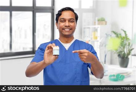 medicine, profession and healthcare concept - happy smiling doctor or male nurse holding jar of pills over medical office at hospital background. doctor or male nurse holding medicine