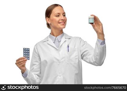 medicine, profession and healthcare concept - happy smiling female doctor comparing pills in jar and pack over white background. smiling female doctor holding medicine pills