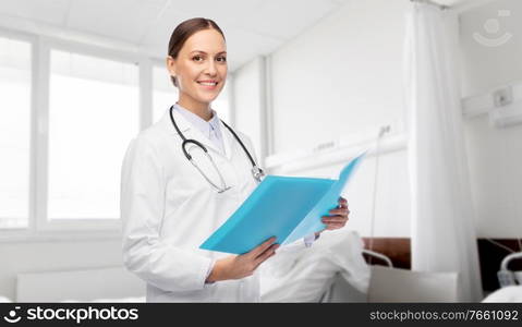 medicine, profession and healthcare concept - happy smiling female doctor in white coat with folder and stethoscope over hospital ward background. smiling female doctor with folder at hospital