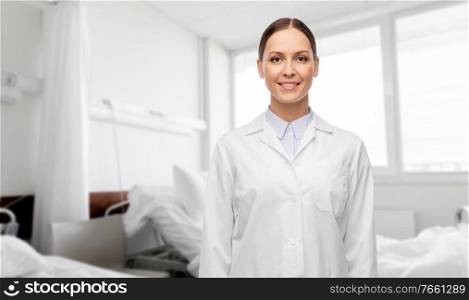 medicine, profession and healthcare concept - happy smiling female doctor in white coat over hospital ward background. smiling female doctor in white coat at hospital