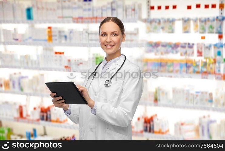 medicine, profession and healthcare concept - happy smiling female doctor in white coat with tablet pc computer and stethoscope over pharmacy background. happy female doctor with tablet pc and stethoscope