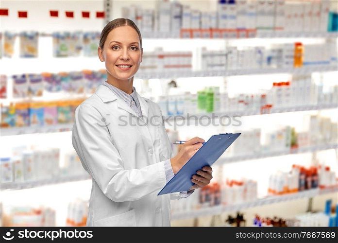 medicine, profession and healthcare concept - happy smiling female doctor or pharmacist in white coat with clipboard and pen writing medical report over pharmacy background. smiling female doctor with clipboard at pharmacy