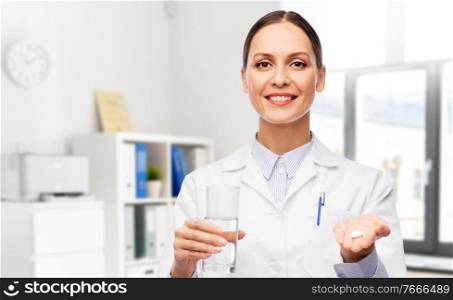 medicine, profession and healthcare concept - happy smiling female doctor with pill and glass of water over hospital background. female doctor with medicine and glass of water