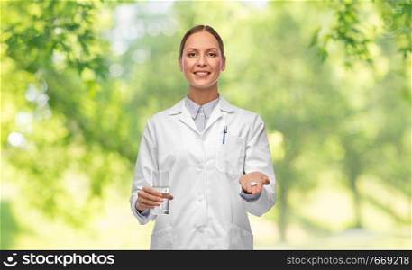 medicine, profession and healthcare concept - happy smiling female doctor with pill and glass of water over green natural background. doctor with medicine and glass of water