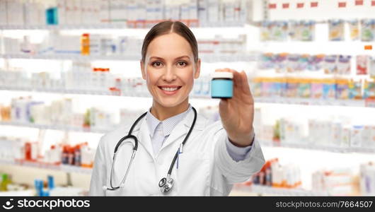 medicine, profession and healthcare concept - happy smiling female doctor with stethoscope holding jar of pills over pharmacy background. smiling female doctor holding jar of medicine