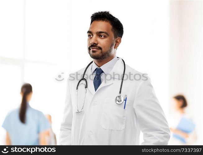 medicine, profession and healthcare concept - indian male doctor in white coat with stethoscope over hospital background. indian male doctor with stethoscope